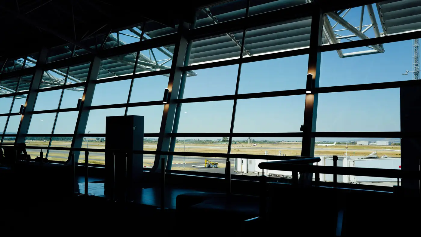View from inside an airport terminal overlooking the runway under a bright blue sky.
