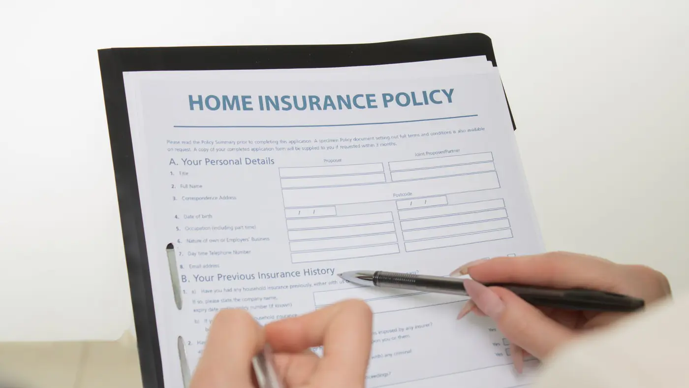 Hands holding pens filling out a home insurance policy document for coverage details.