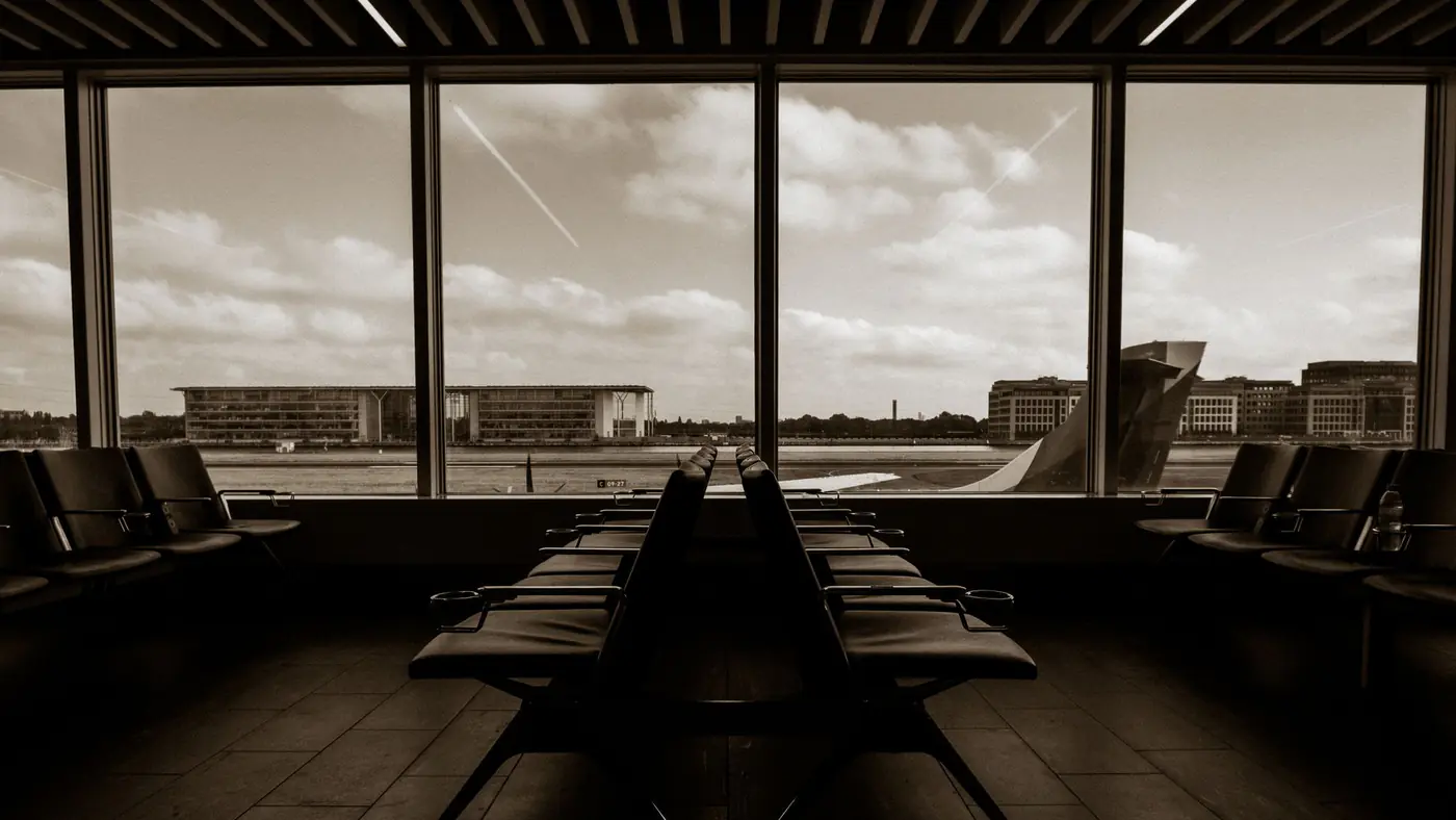 Quiet airport terminal in sepia tone overlooking runway and airplane wing.