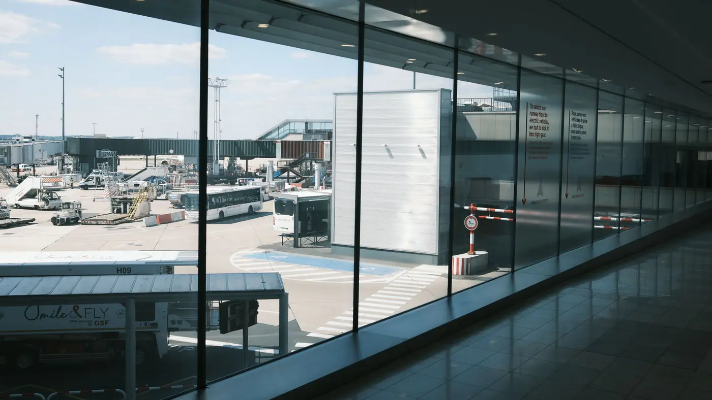 Wide view of an airport terminal hallway and tarmac, showcasing airplanes and buses.