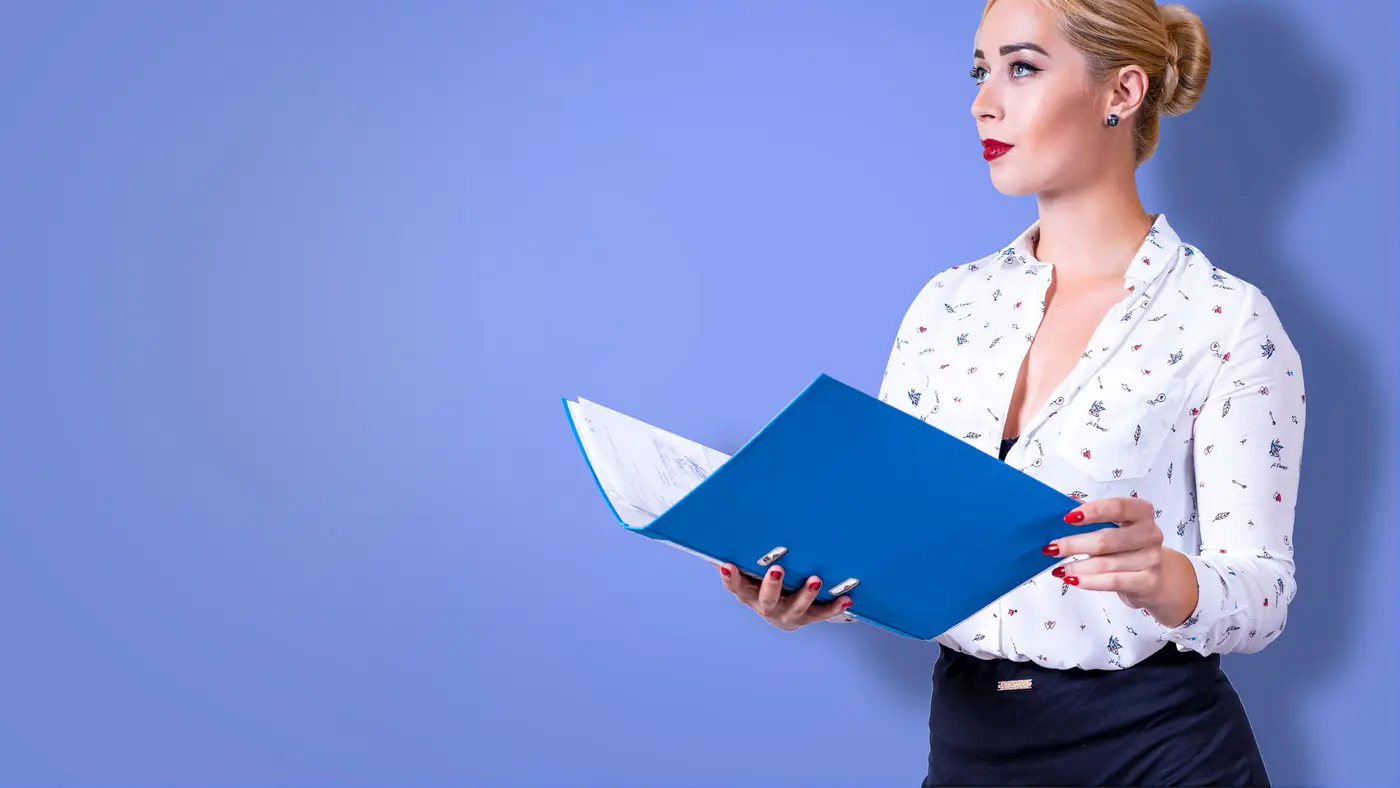 Professional businesswoman standing with a blue folder against a blue background.