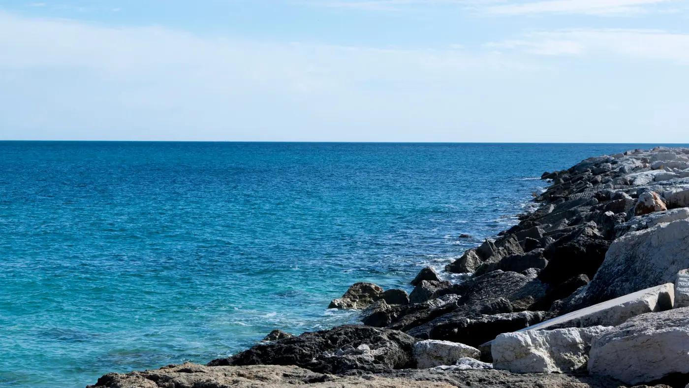 Peaceful seascape featuring rocky coastline and clear blue water under a sunny sky.