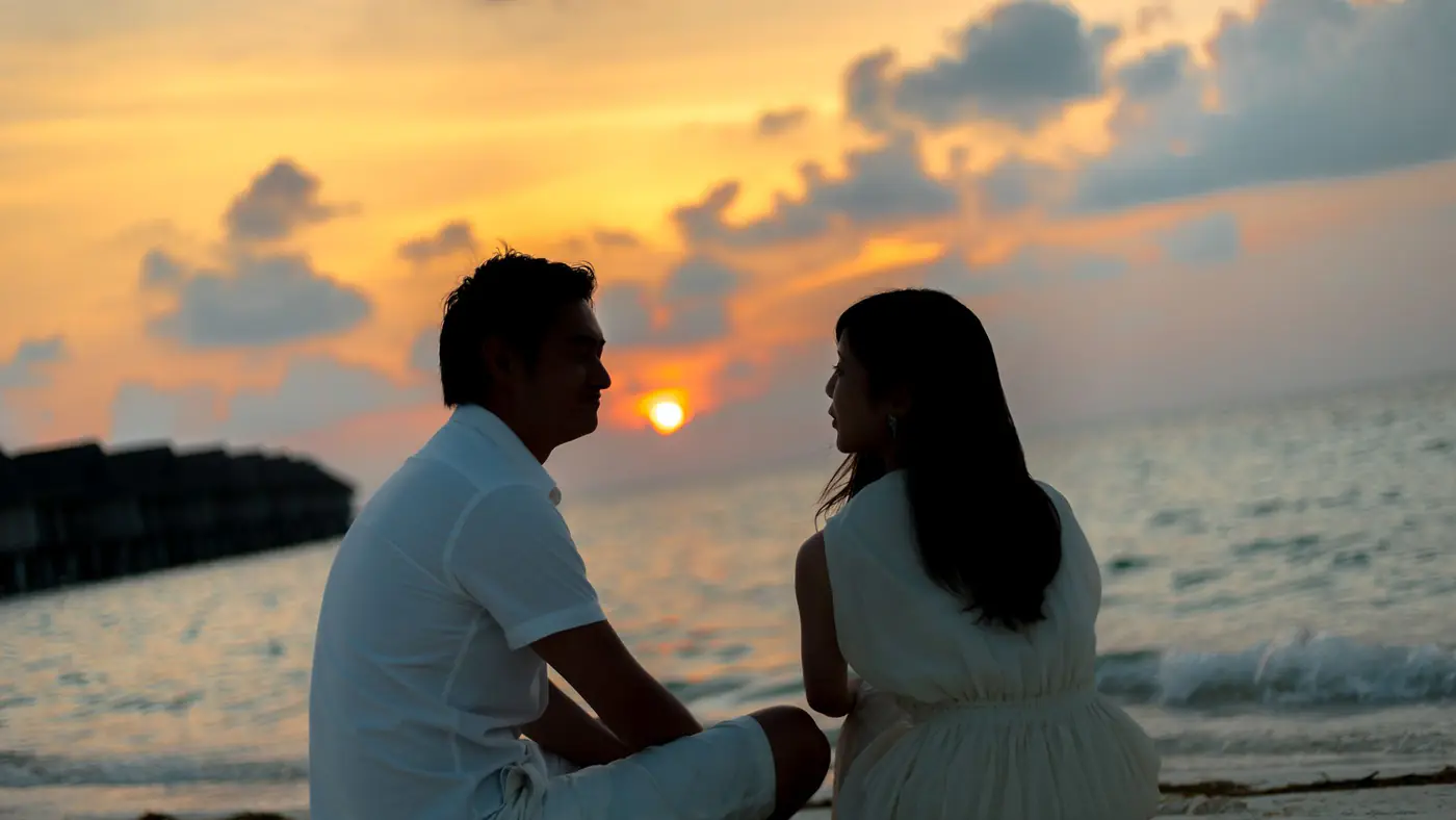 A couple sitting on a sandy beach, enjoying a beautiful sunset over the ocean.