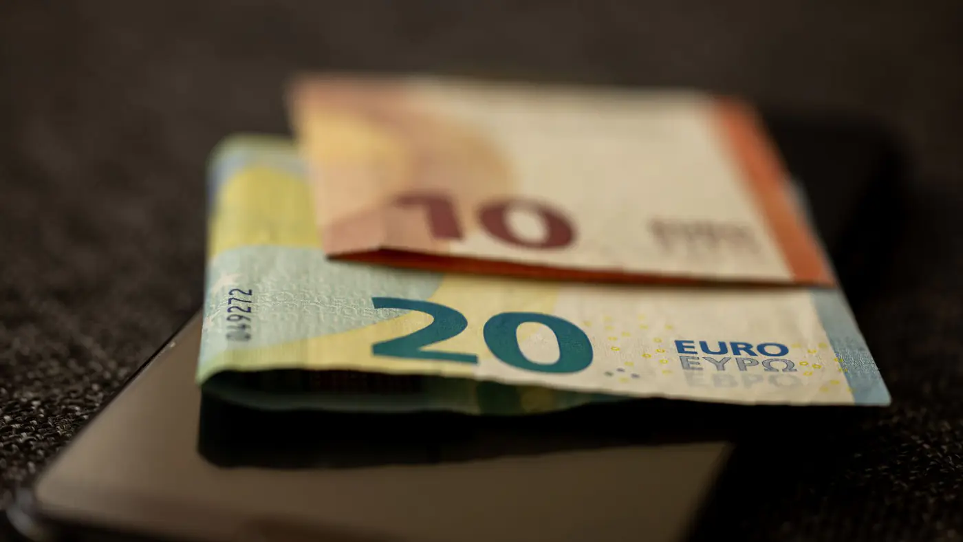 A detailed close-up shot of 10 and 20 euro banknotes placed on a smartphone, representing finance and technology.