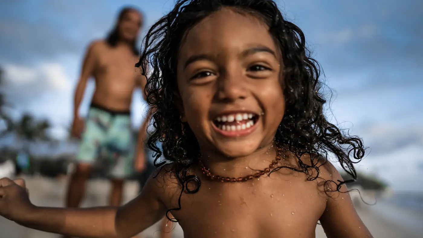 A happy child with curly hair playing on a tropical beach in the summer.