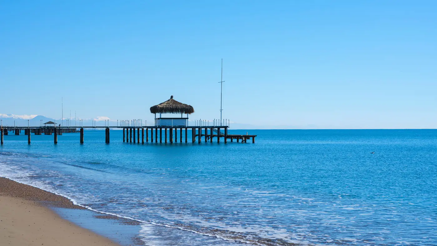 Scenic view of an ocean pier with a hut against clear blue skies and turquoise water.