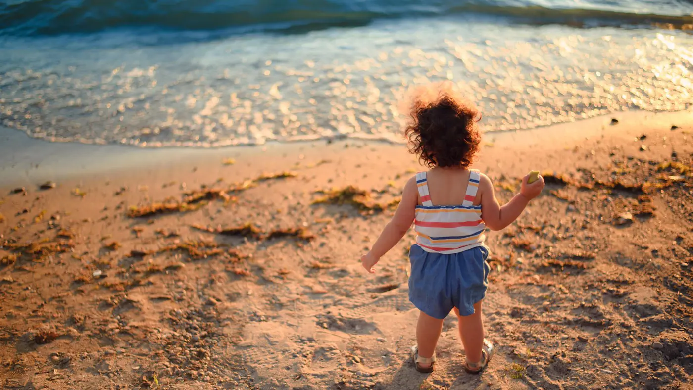 A toddler enjoying a beach outing at sunset with flowing waves and sandy shore.