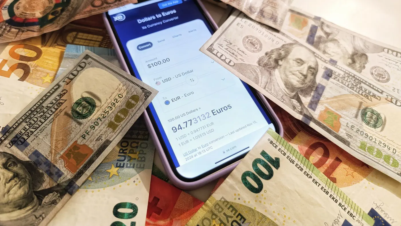A smartphone displaying a currency converter surrounded by dollar and euro banknotes, highlighting exchange rates.