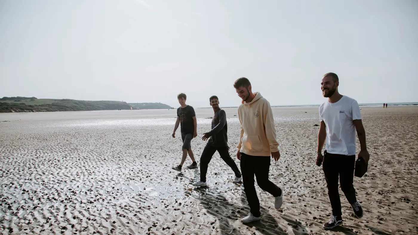 Full length of cheerful adult males chatting while strolling together on empty seashore in sunlight