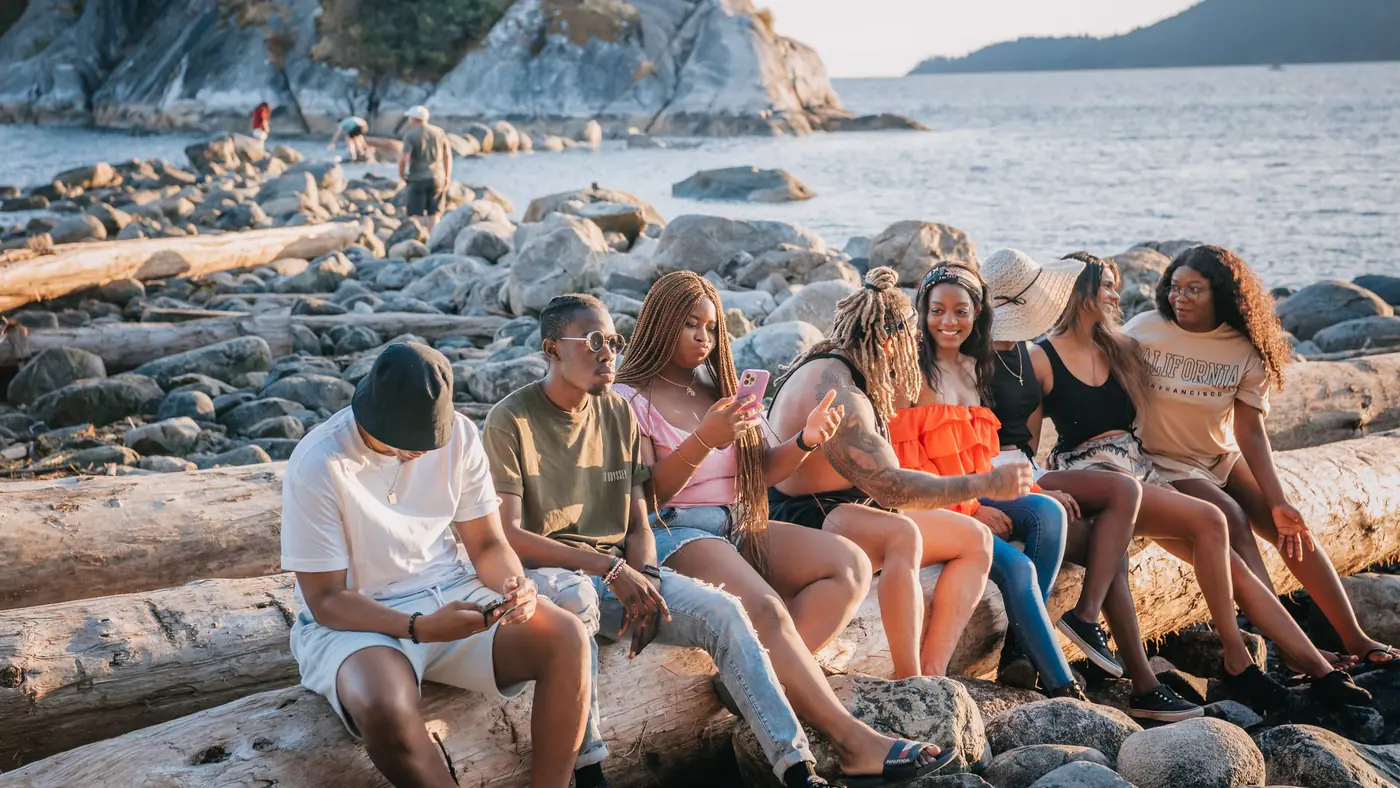 A group of friends relax on a rocky beach at sunset, enjoying conversation and a beautiful view.