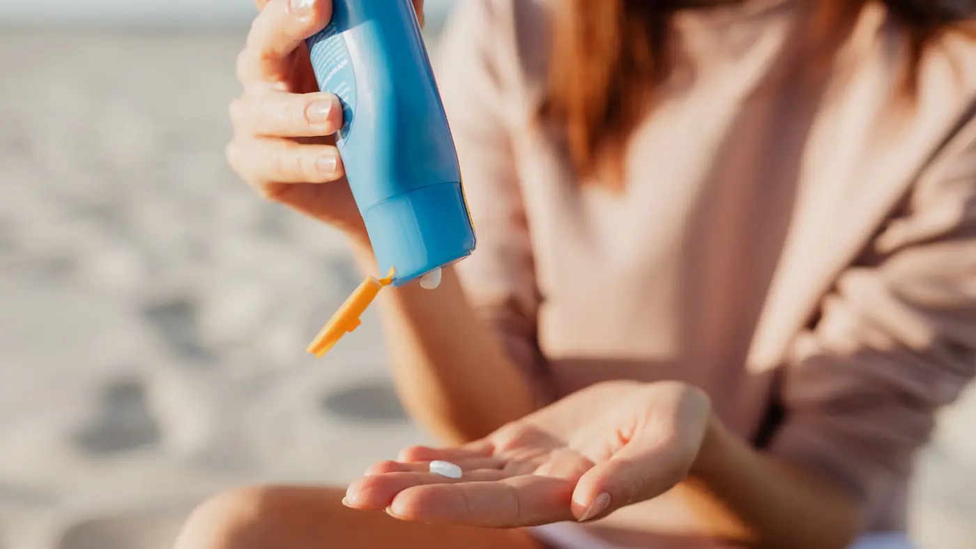 A person applies sunscreen at the beach on a sunny day.