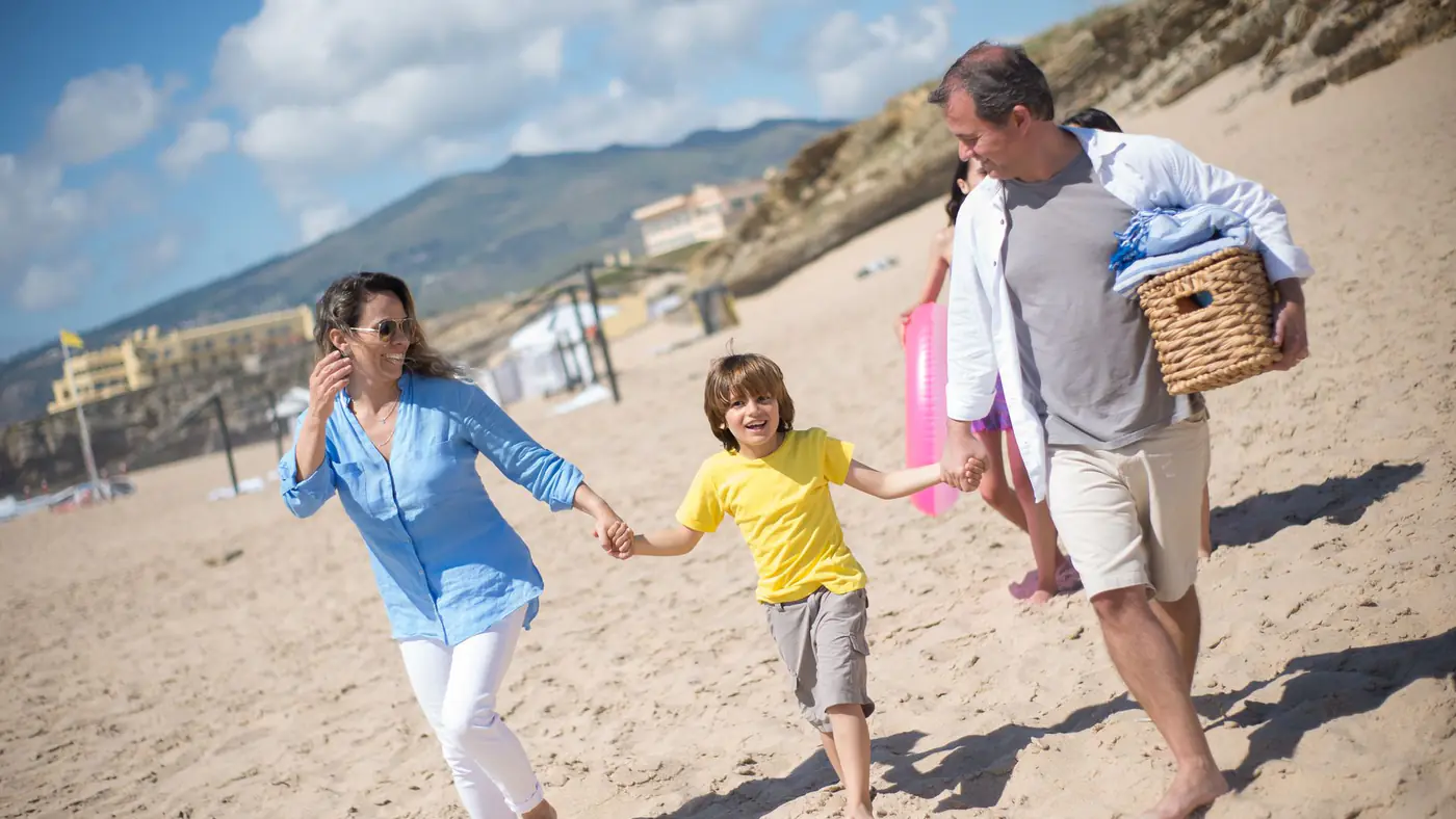 A joyful family strolls along a sunny beach in Portugal, enjoying quality time together.