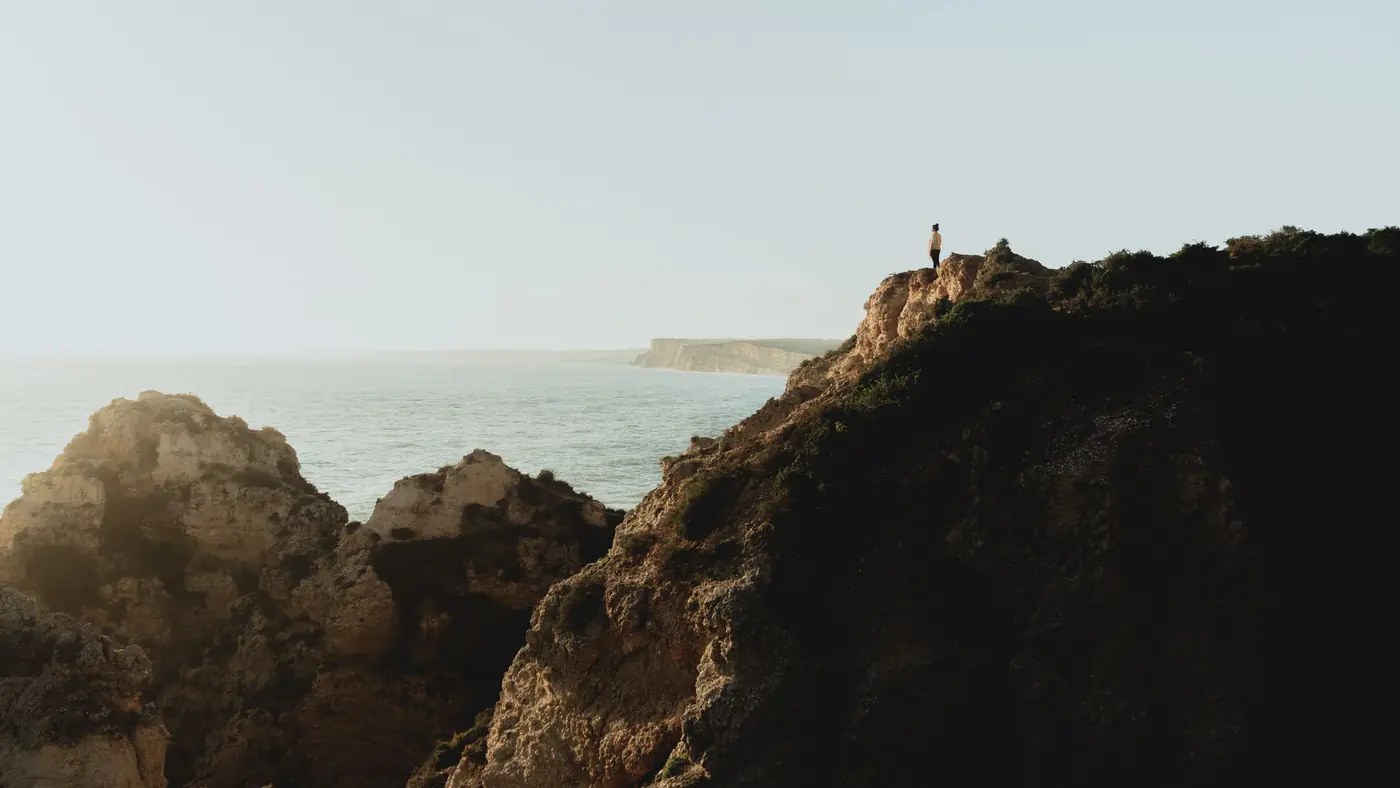 A person stands on a cliff overlooking the ocean in the Algarve region, Portugal.