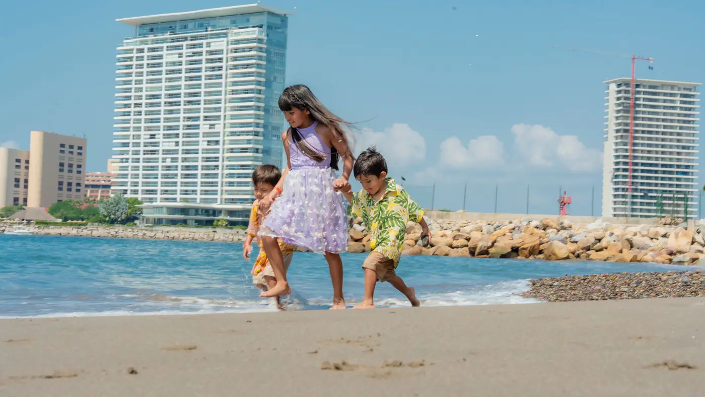 Three children playing on a sunny beach with tall buildings in the background, capturing summer joy.
