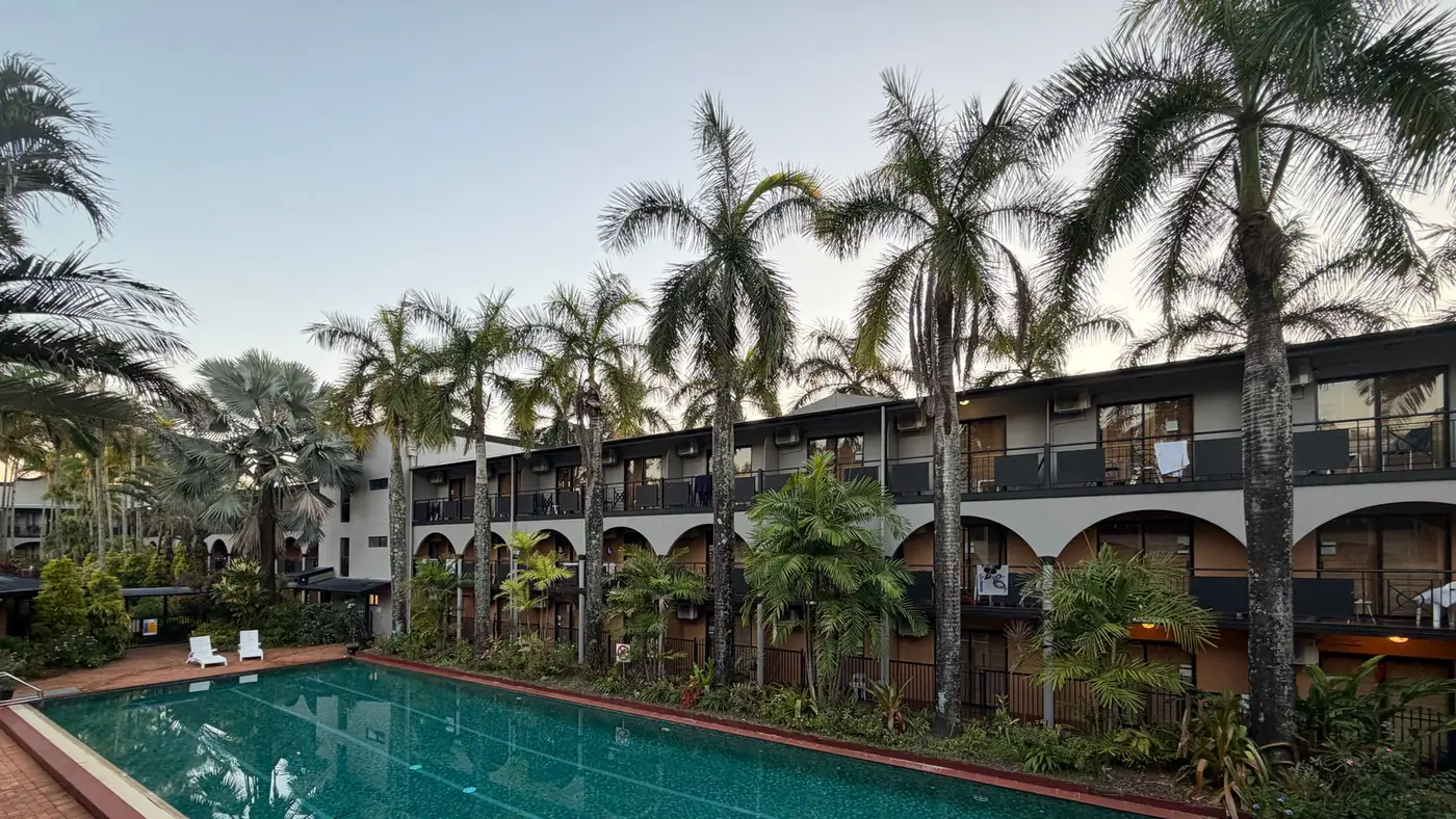 Serene tropical resort with a lush palm-lined swimming pool at sunrise.